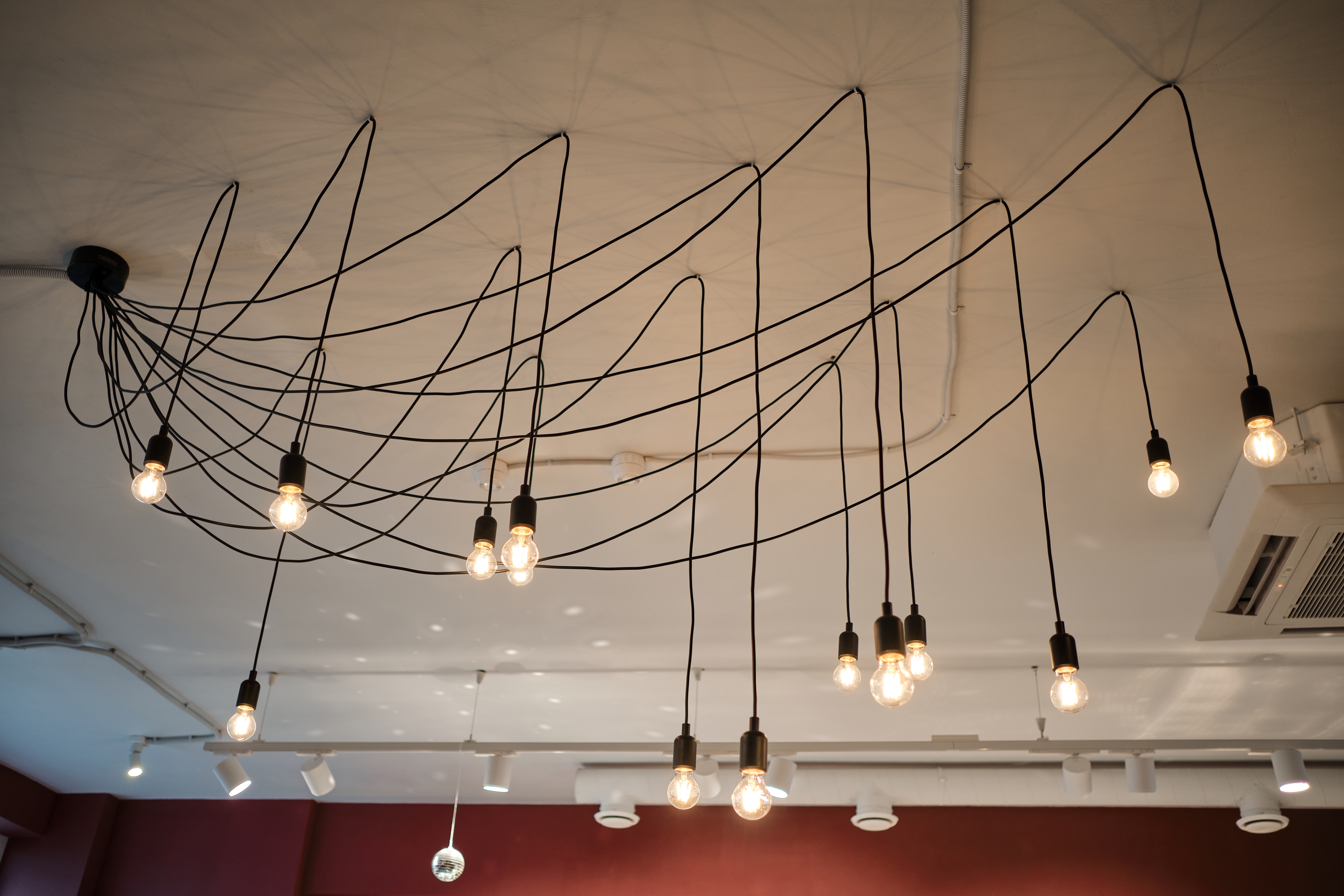Unusual chandelier with individual light bulbs adorns ceiling in cozy cafe. Lamps illuminate large